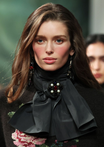A model with long light brown hair wearing a sweather and black scarf